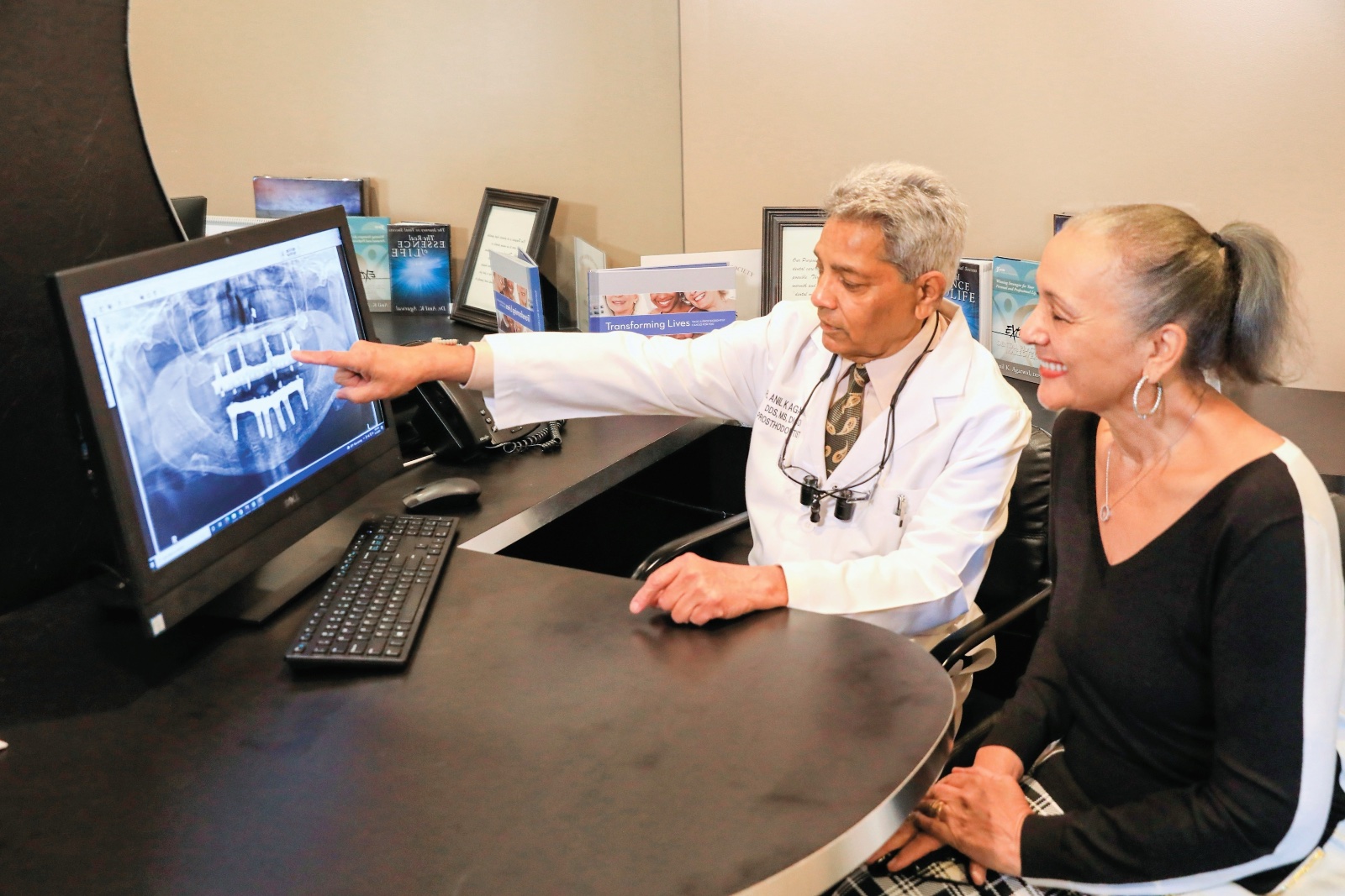 A dentist shows a patient a teeth x-ray on a computer screen