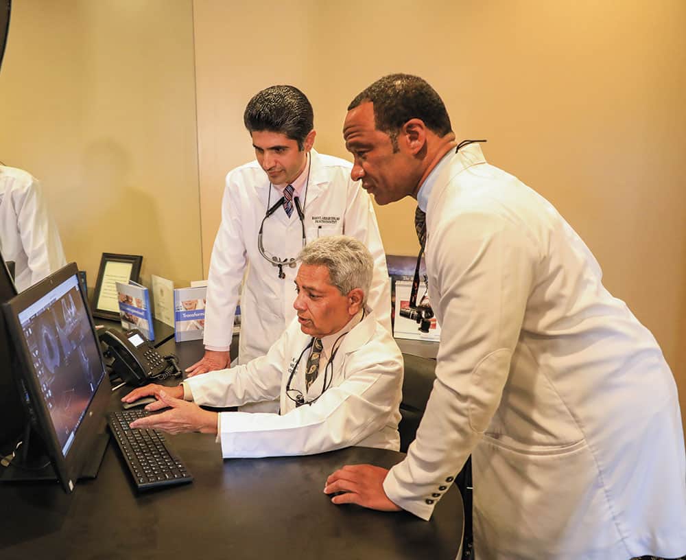 Three doctors working at a computer discussing some X-ray imagery of dental structures in the mouth.
