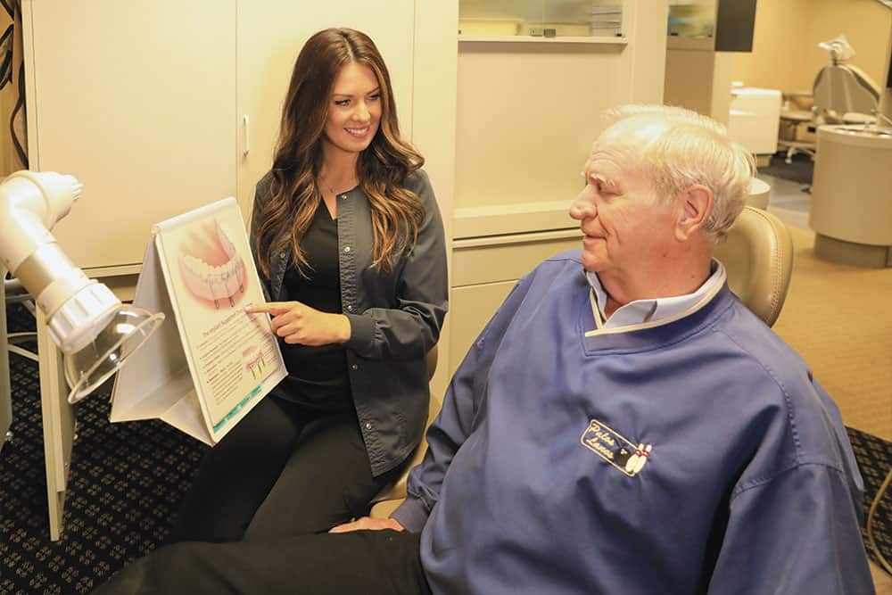 Dental assistant presenting a pamphlet to a patient about full-mouth reconstruction dental treatments.