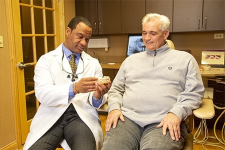 Dr. showing patient a model of teeth during a dental implant consultation.