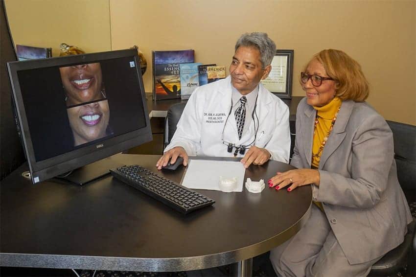 Dr. Anil Agarwal and a patient examine a before and after image of a smile on a computer screen during a full-mouth reconstruction consultation.